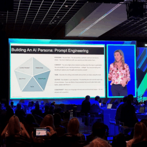 A conference with an image of a slideshow and a woman speaking projected onto a large screen.