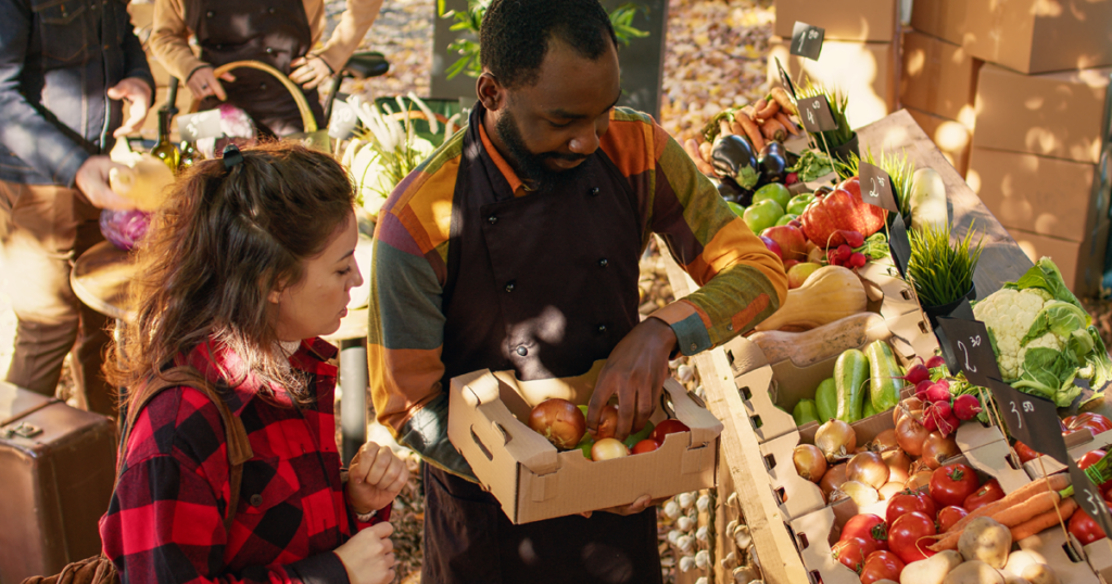 Vendor helping a customer select fresh produce at an outdoor market.
