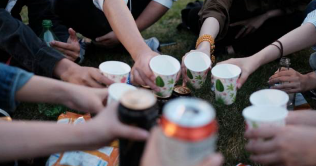 Group of people raising paper cups together outdoors in a toast.
