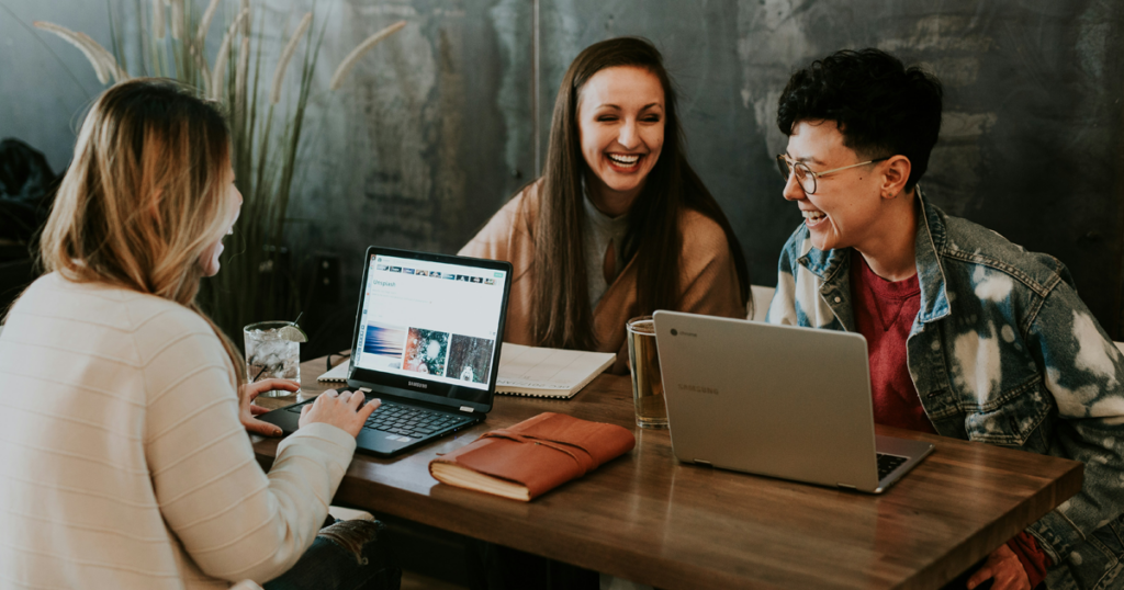 Three people sitting at a table with laptops, talking and working together.