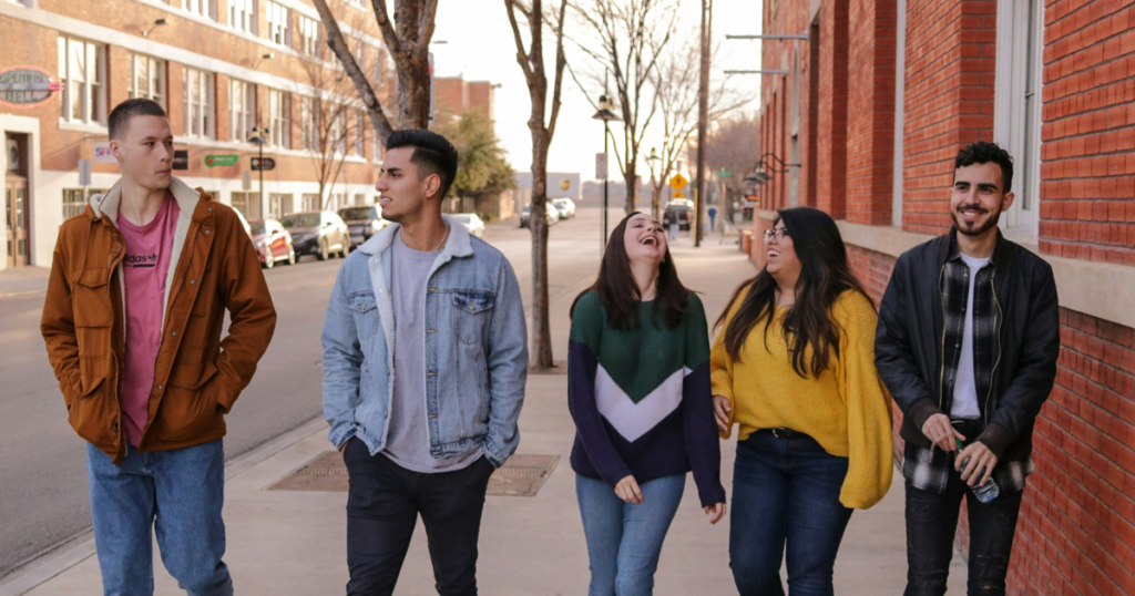 Five people walking together on a city sidewalk next to brick buildings.