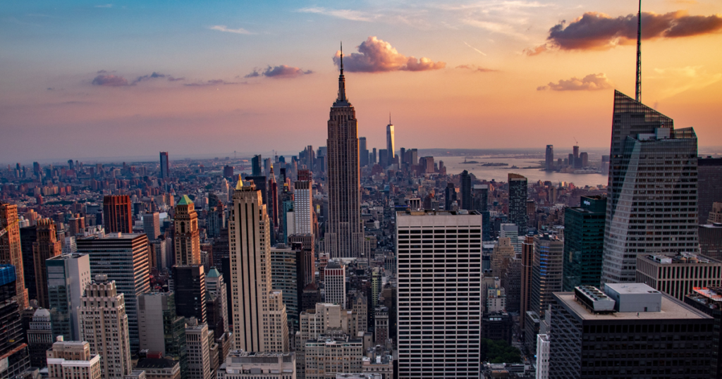 View of the New York City skyline at sunset, featuring the Empire State Building in Midtown Manhattan.