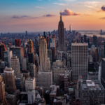 View of the New York City skyline at sunset, featuring the Empire State Building in Midtown Manhattan.