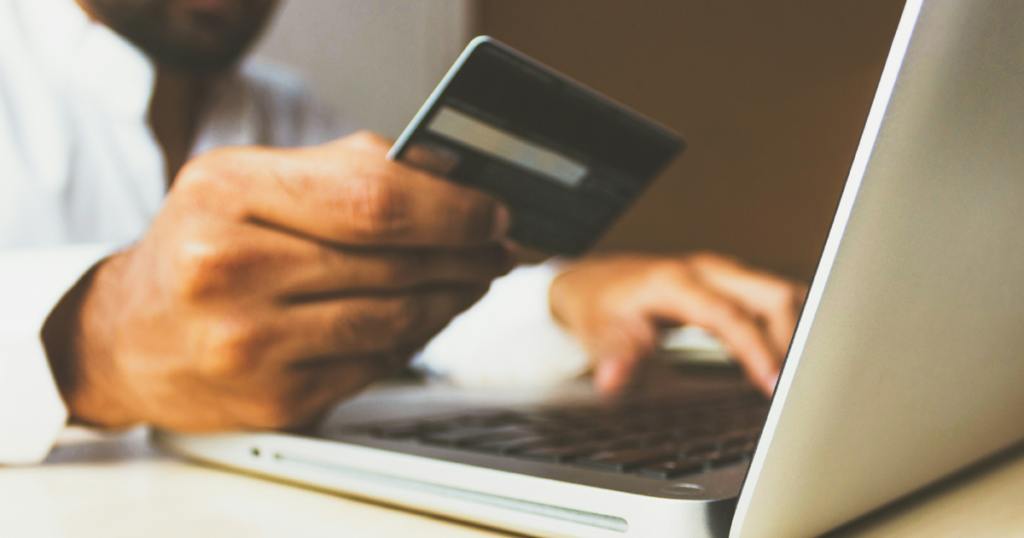 A person holding a credit card while using a laptop to make a purchase online.